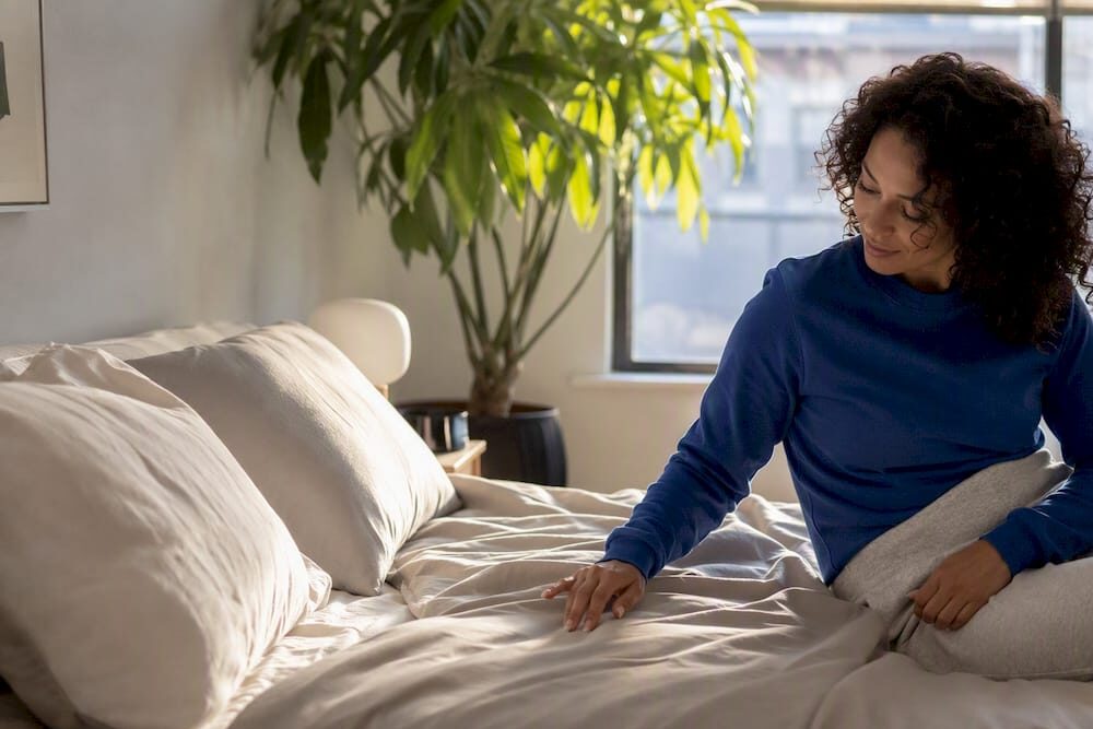 Woman comparing Parachute and Brooklinen sheets on bed