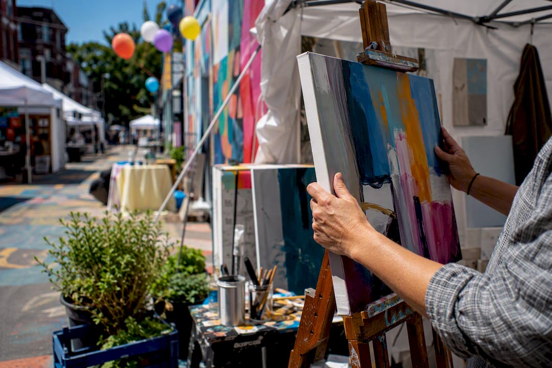 Hands installing artwork at outdoor urban art fair booths
