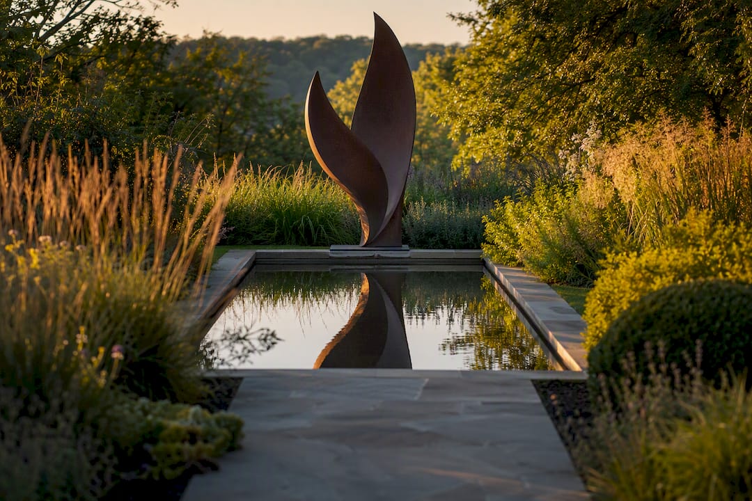 Metal garden sculpture reflected in still water